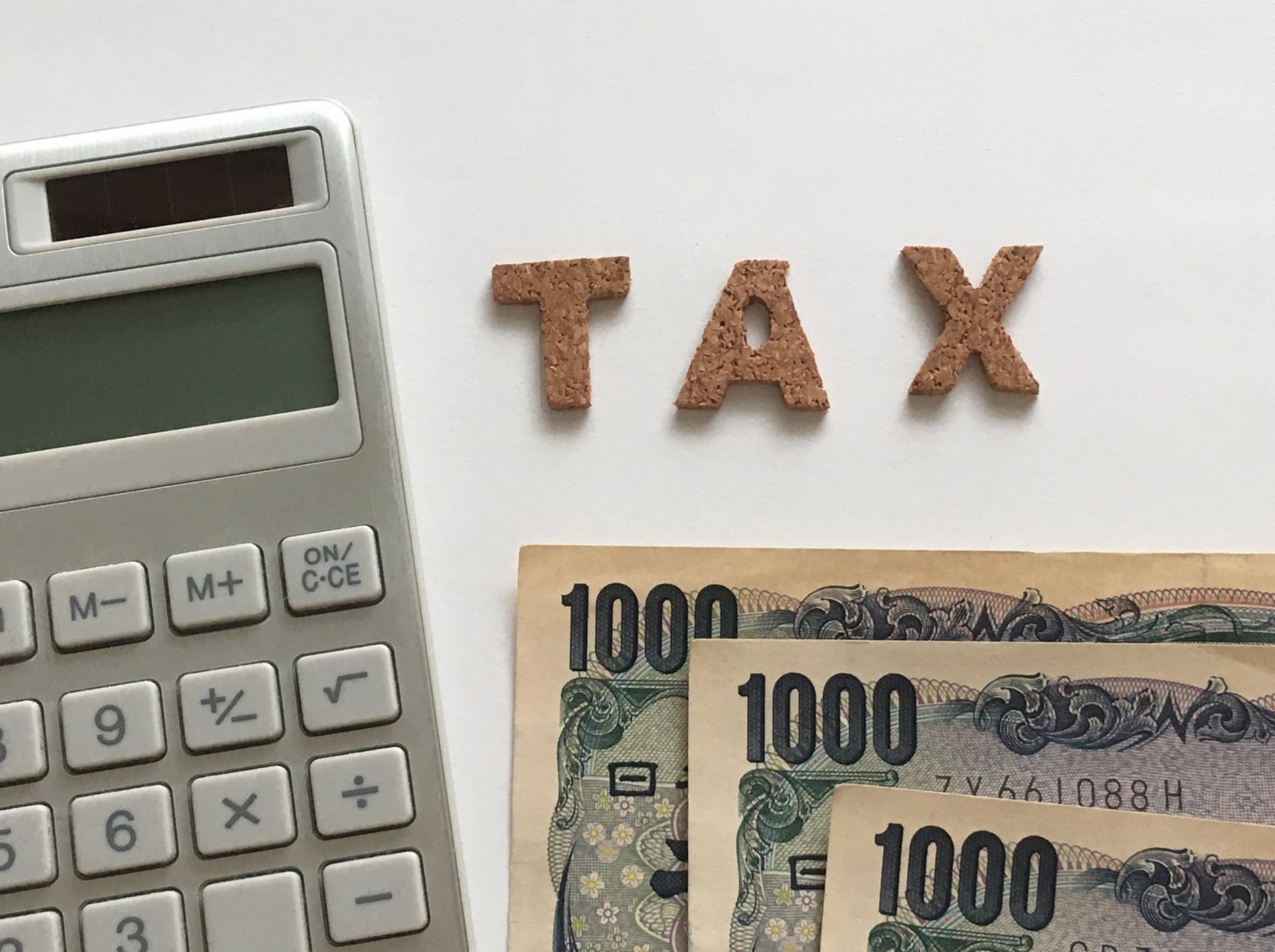 電卓と紙幣の横に「TAX」の文字を並べた様子
